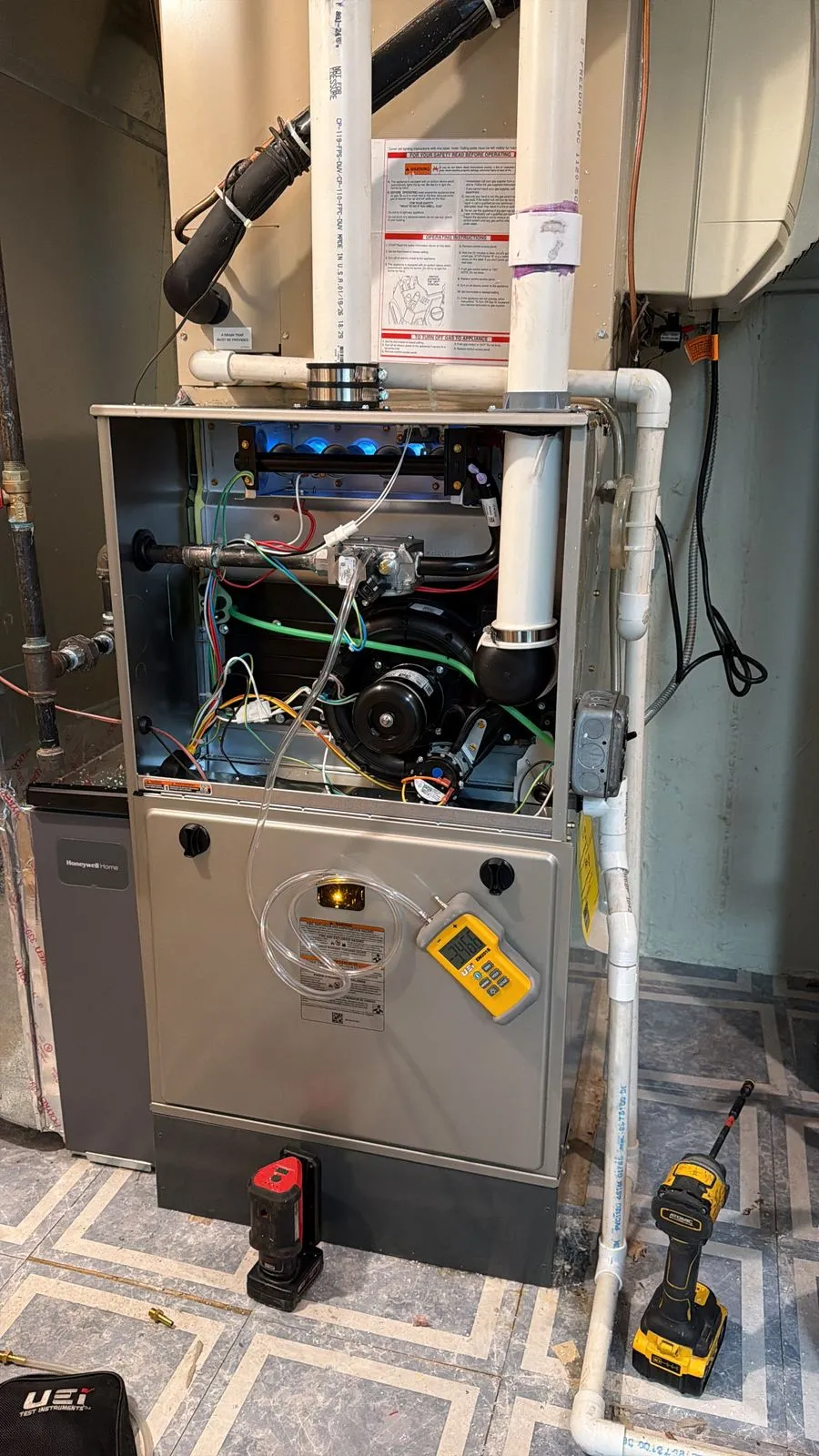 The same furnace with its upper panel off during start-up, the row of burners lit blue and a digital manometer hung on the door while the gas pressure is set.