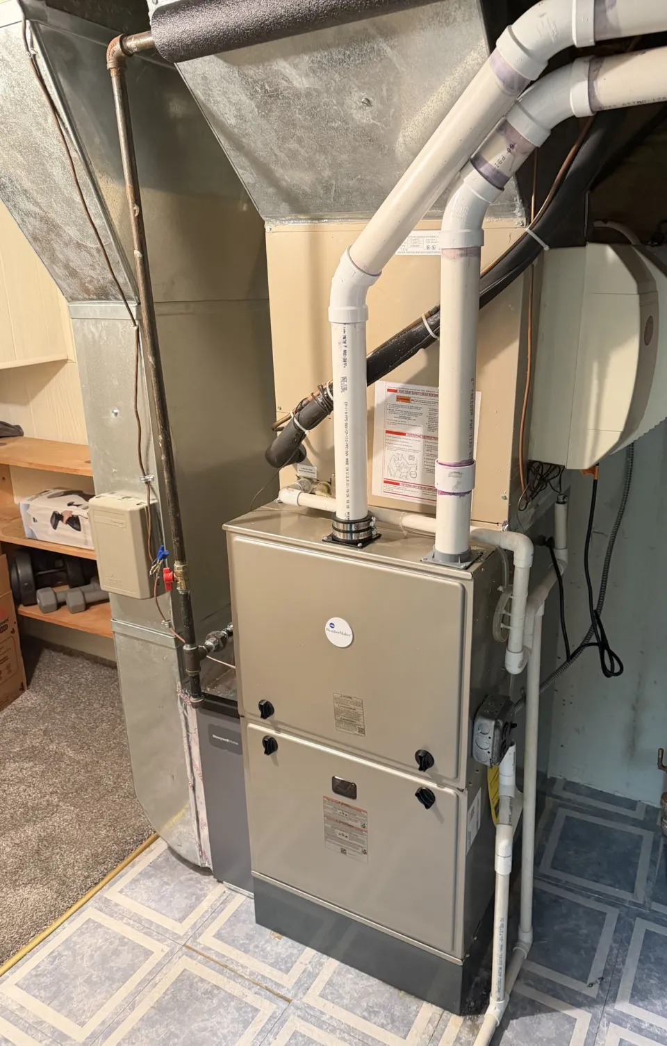 A newly installed high-efficiency gas furnace in a utility closet, its PVC intake and exhaust piping run up to the ceiling, a media filter cabinet on the return side and a bypass humidifier on the wall behind.