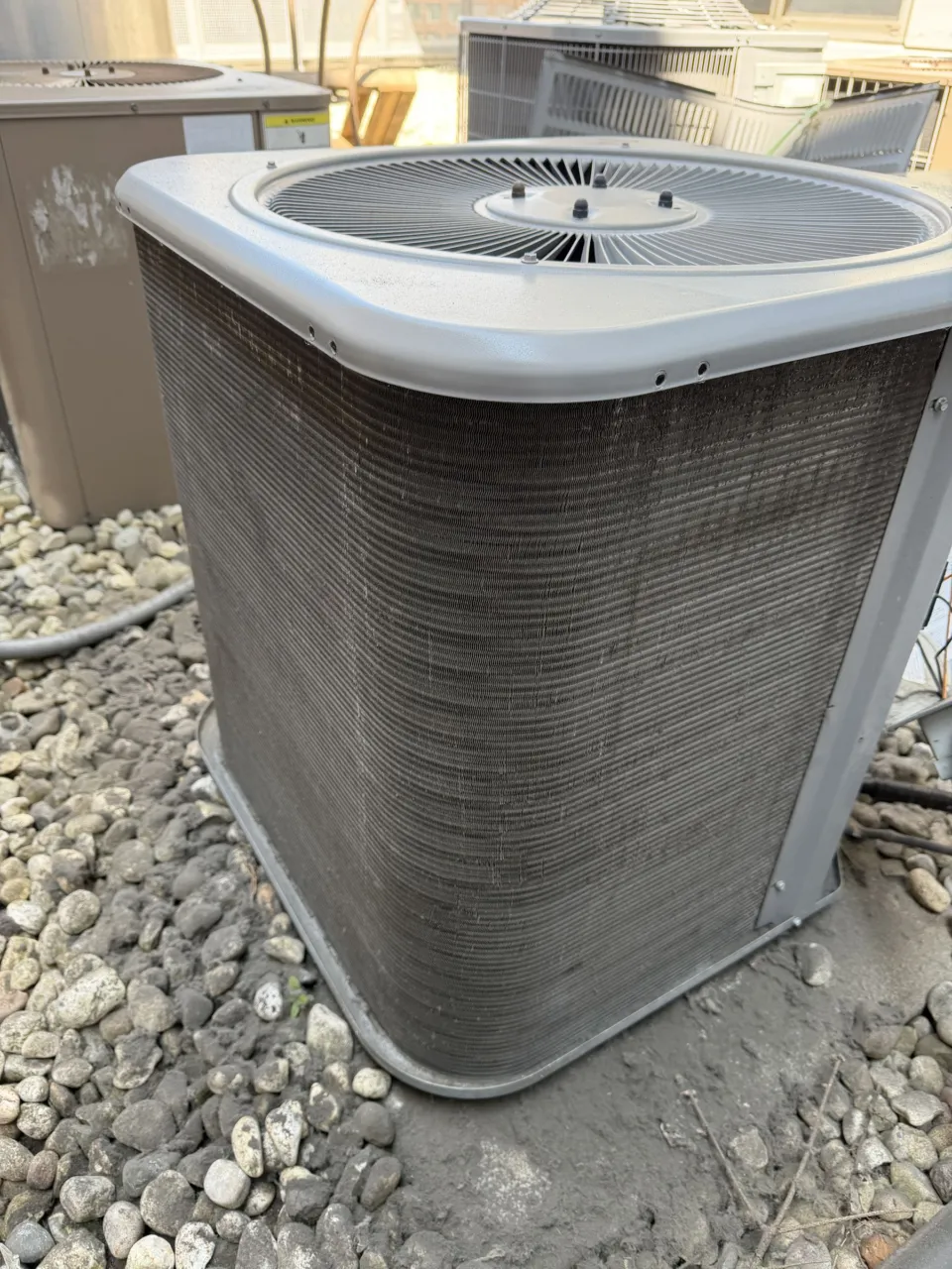 The same outdoor air conditioner after cleaning, with the aluminum fins of the condenser coil visible again.