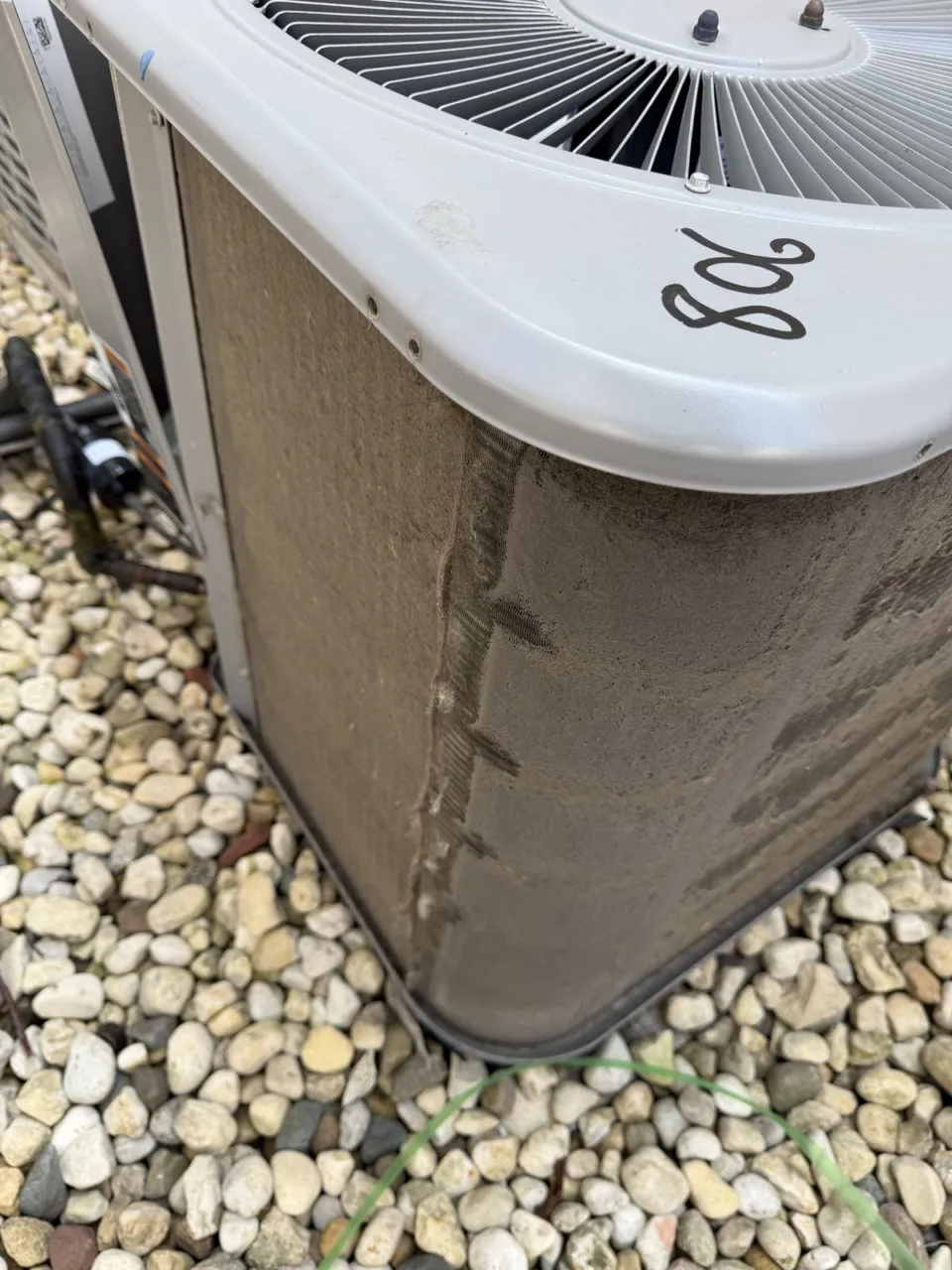 Close-up of a condenser coil corner matted with gray dirt so that no air can pass between the fins.