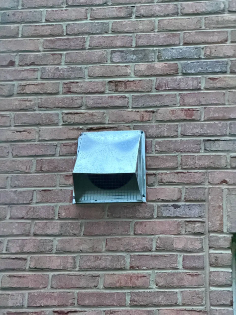 A galvanized make-up air intake hood fixed to a red brick wall, screened against the weather.