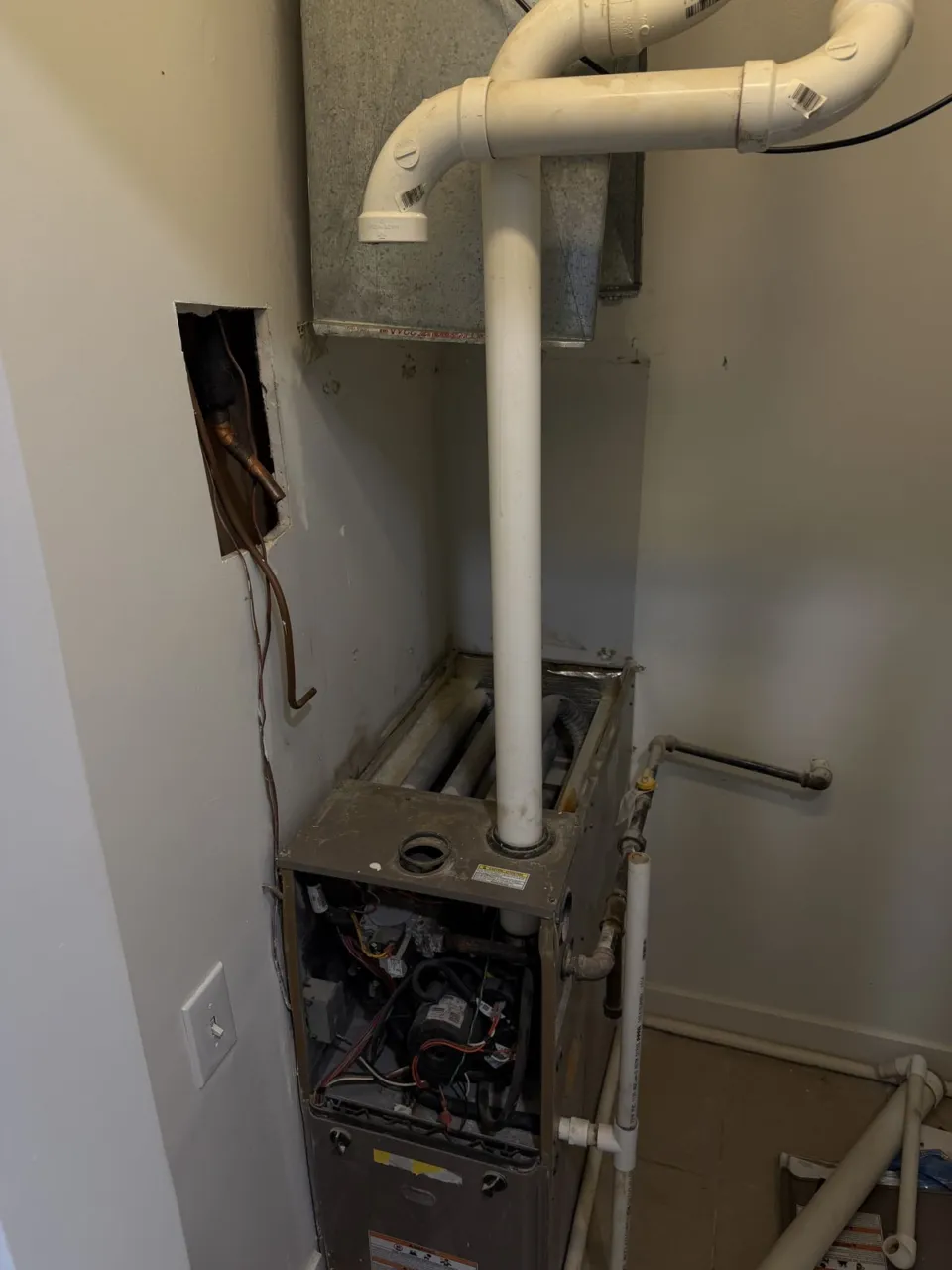 An opened furnace cabinet in a closet with the evaporator coil taken out and the wiring exposed.