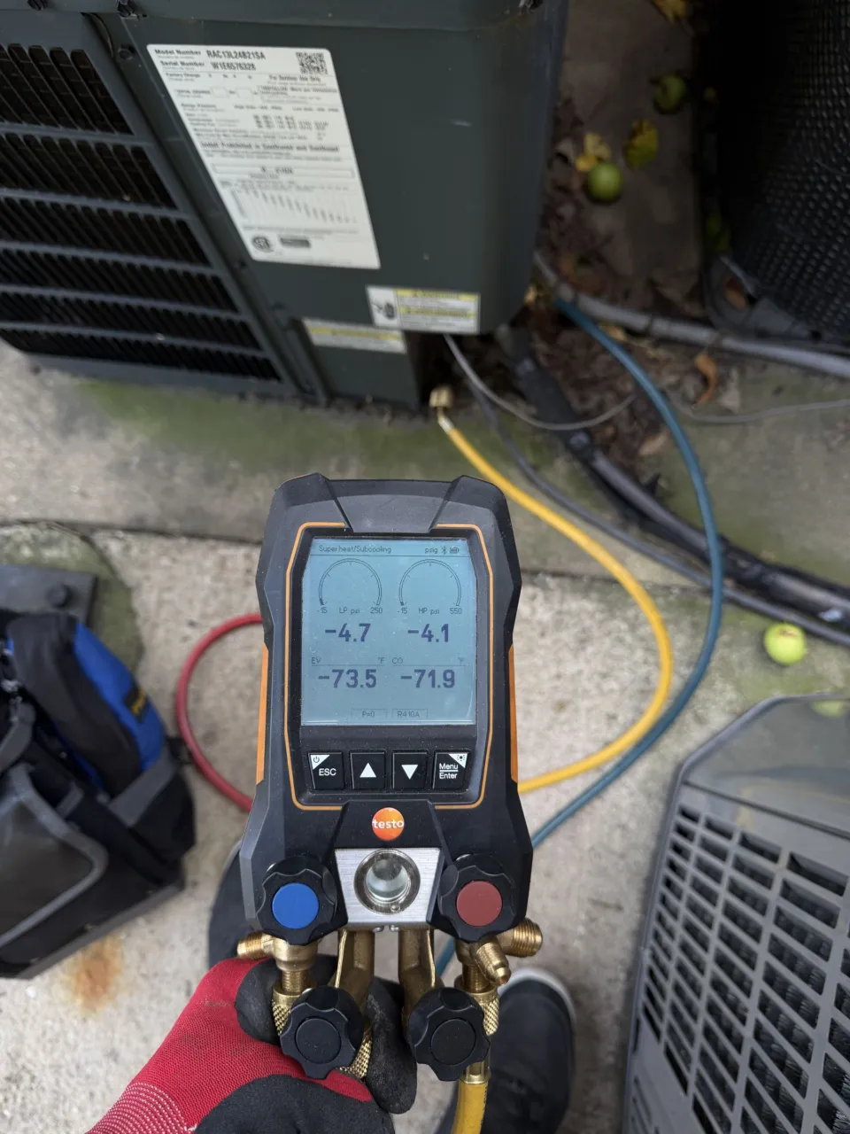 A digital refrigerant manifold connected to an outdoor unit, reading zero pressure on both sides.