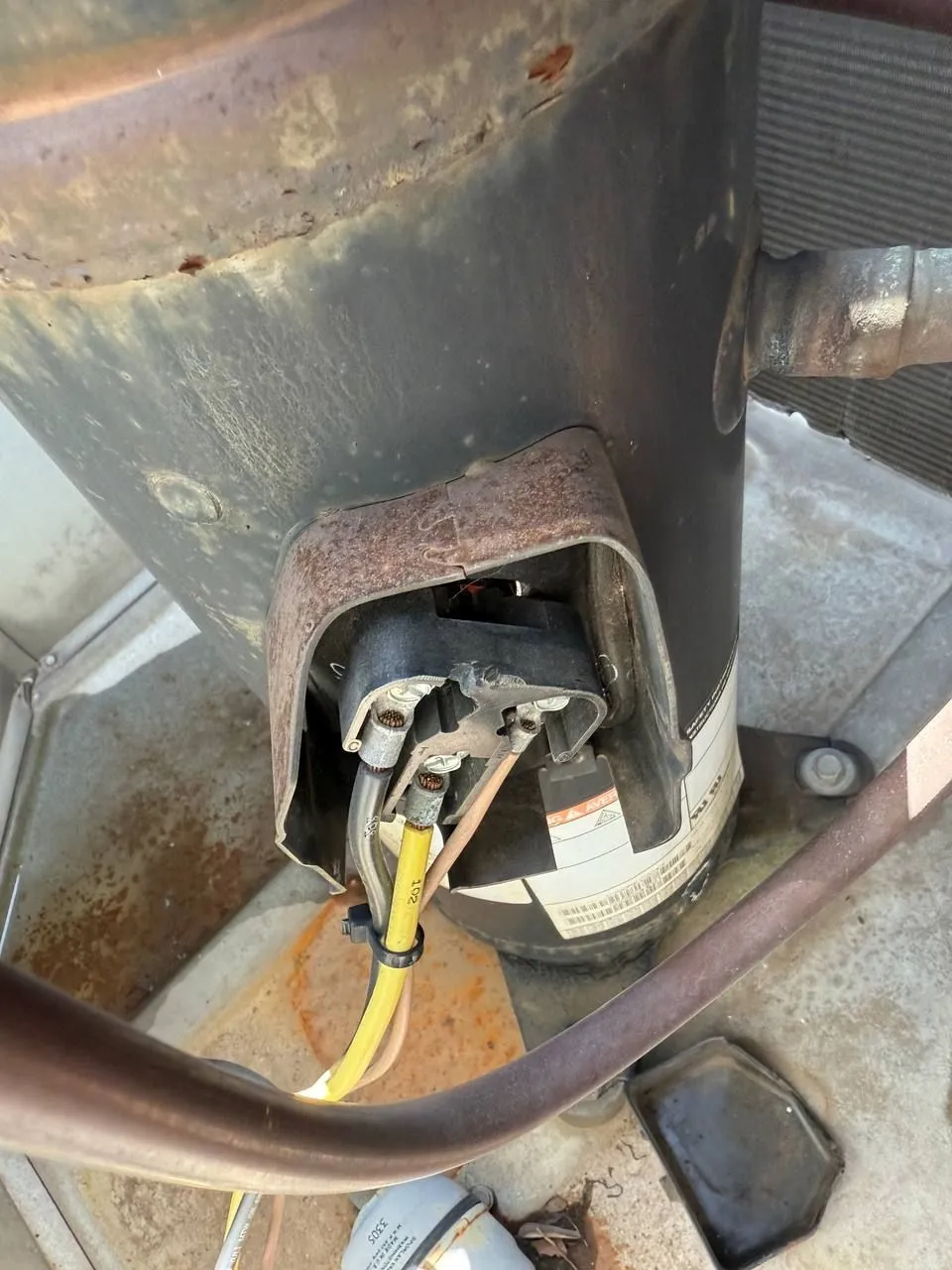 The terminal box of a rooftop unit compressor with its cover opened, showing the wiring connections on the compressor shell.