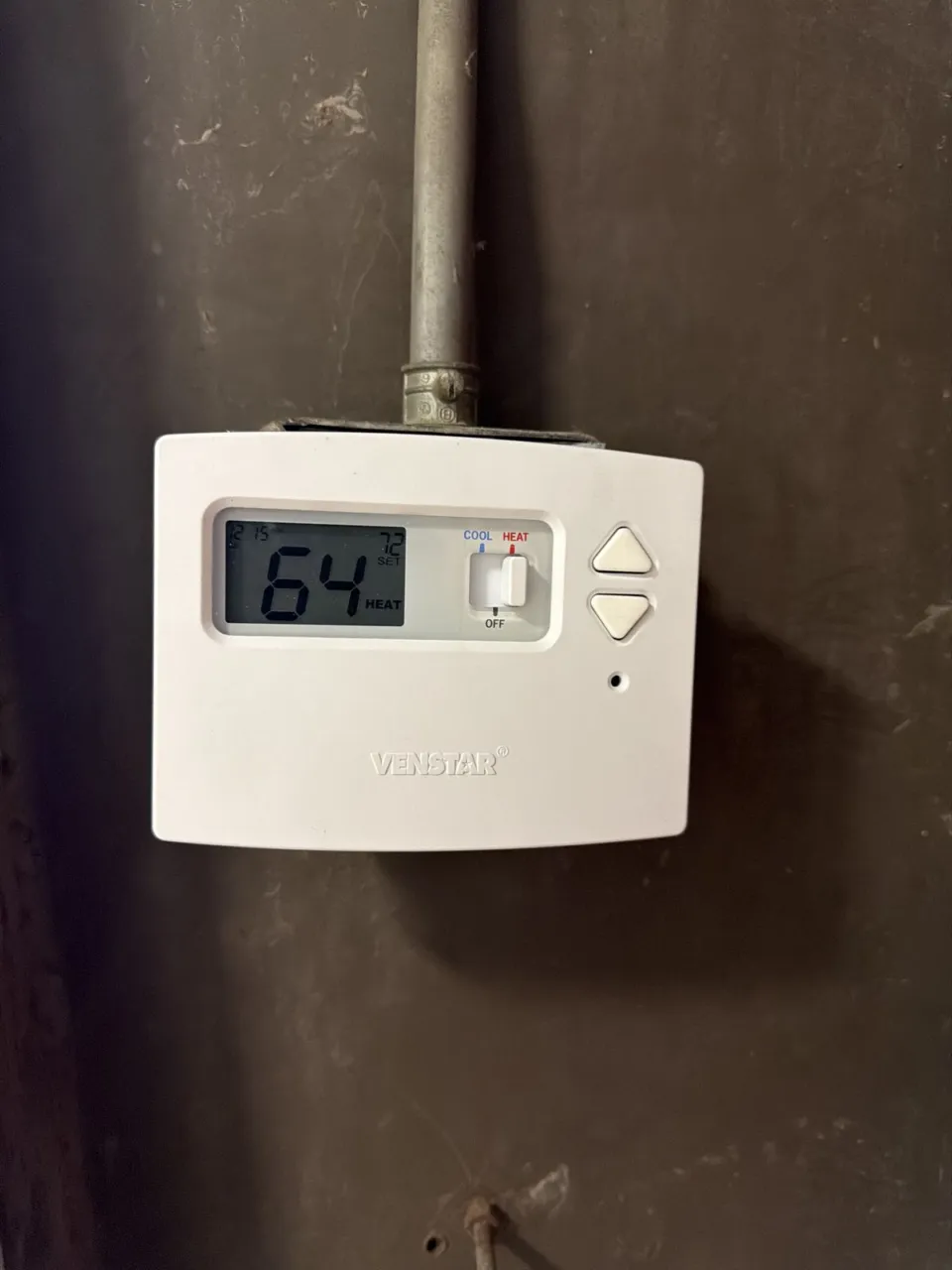 A Venstar thermostat mounted on a concrete column below the heater's conduit, reading 64 F with the set point at 72 F and the switch on heat.