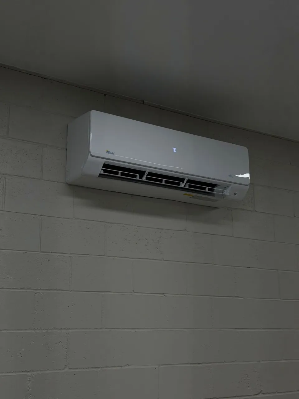 A Senville wall-mounted indoor unit high on a painted block wall, its display lit.
