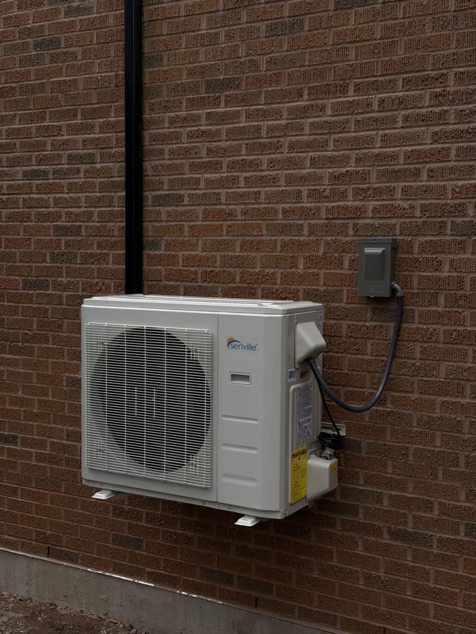 A new Senville outdoor unit on wall brackets against a brick wall, its power cable run to an electrical box beside it.