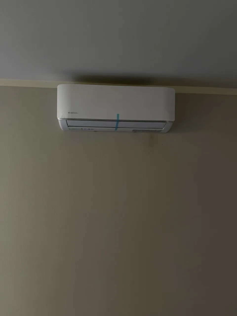 A MrCool wall-mounted indoor head installed high on a bare wall just below the ceiling, its louver closed.