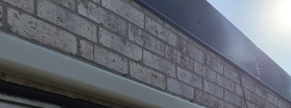 The white line set cover of the mini-split running along a light brick wall under the roof edge.