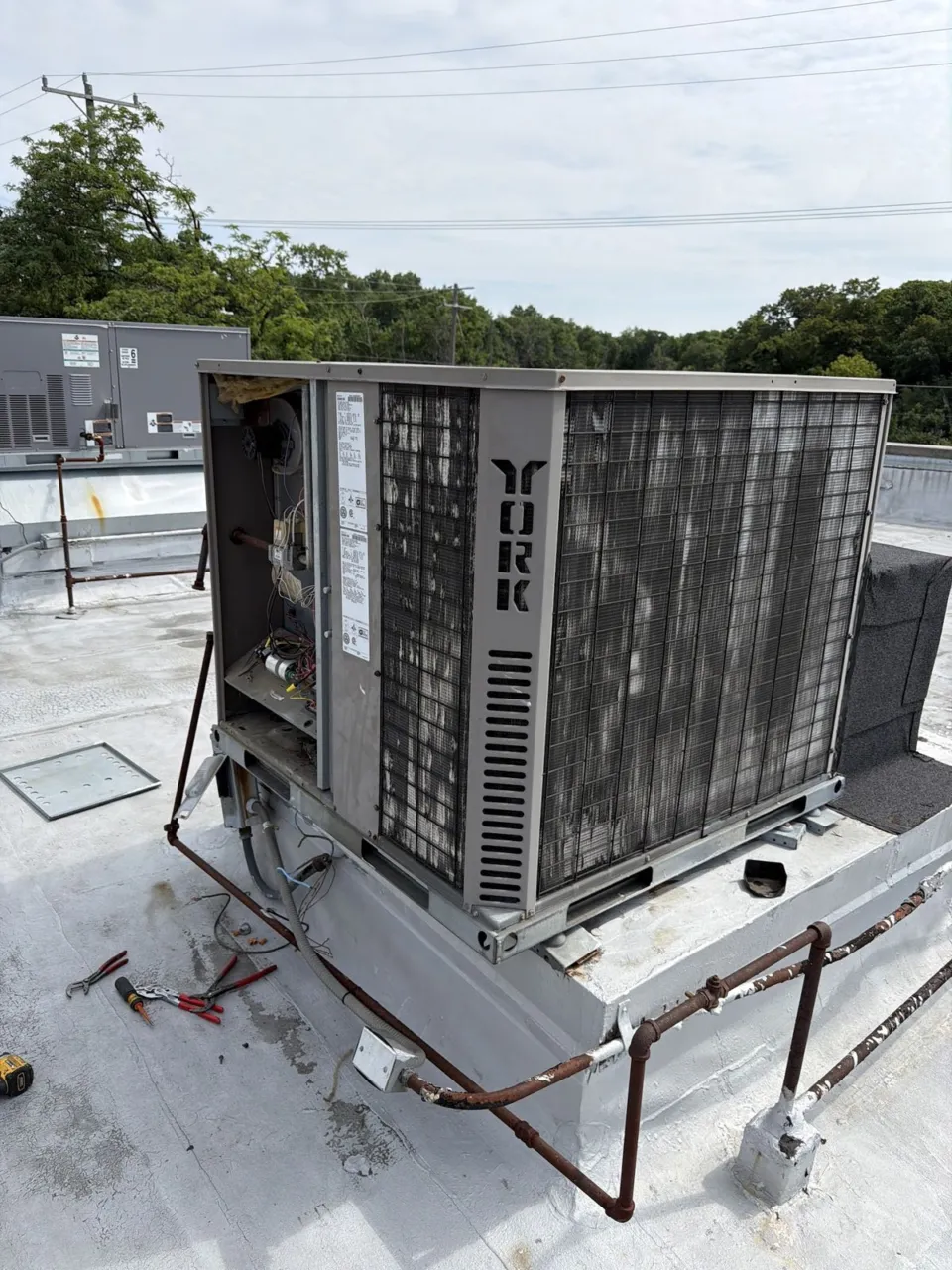 A rooftop unit with its service panels open showing the blower and wiring, tools laid out on the roof.